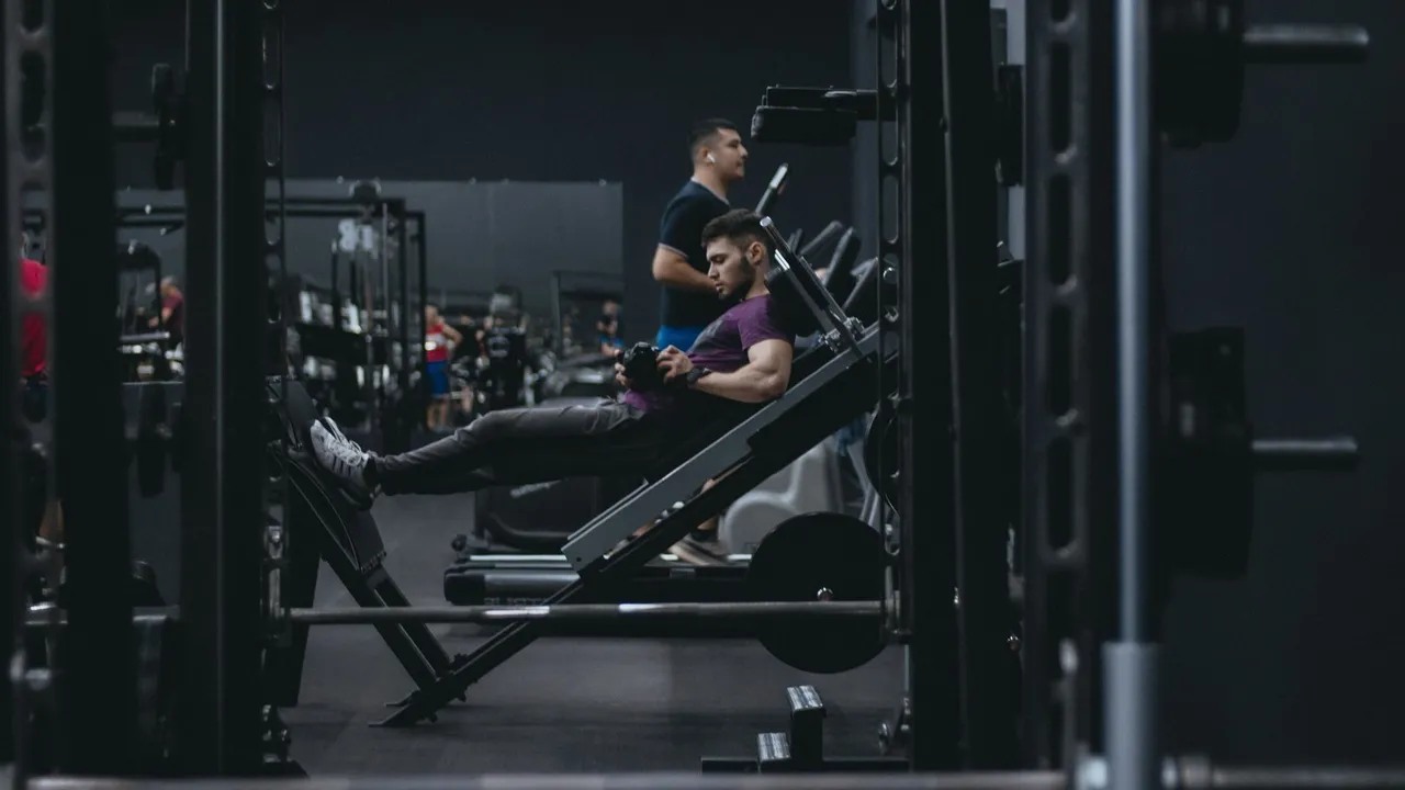Homme assis sur une machine de leg extension, galet posé au bas du tibia, en salle de sport